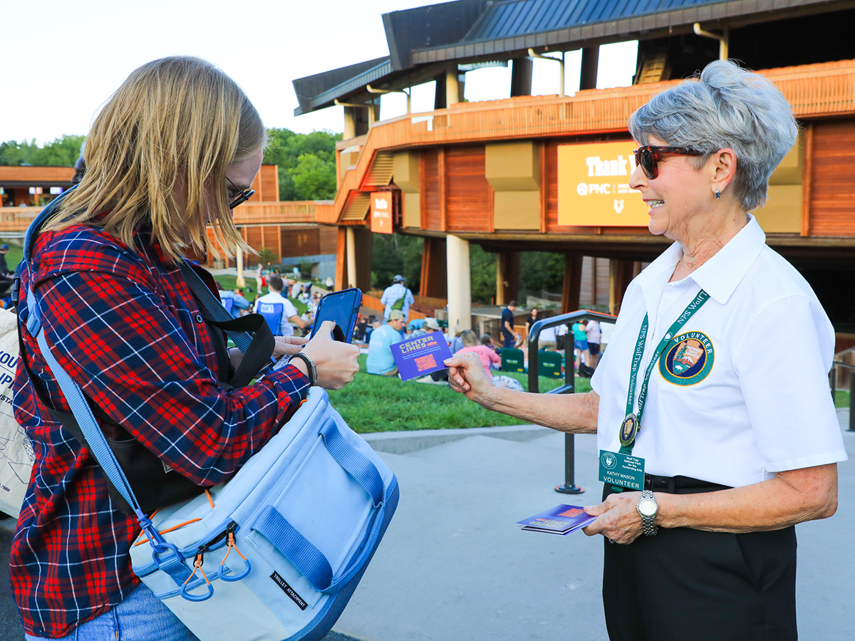 Senior volunteer hands out event flyers and welcomes guests with a smile at a community gathering.