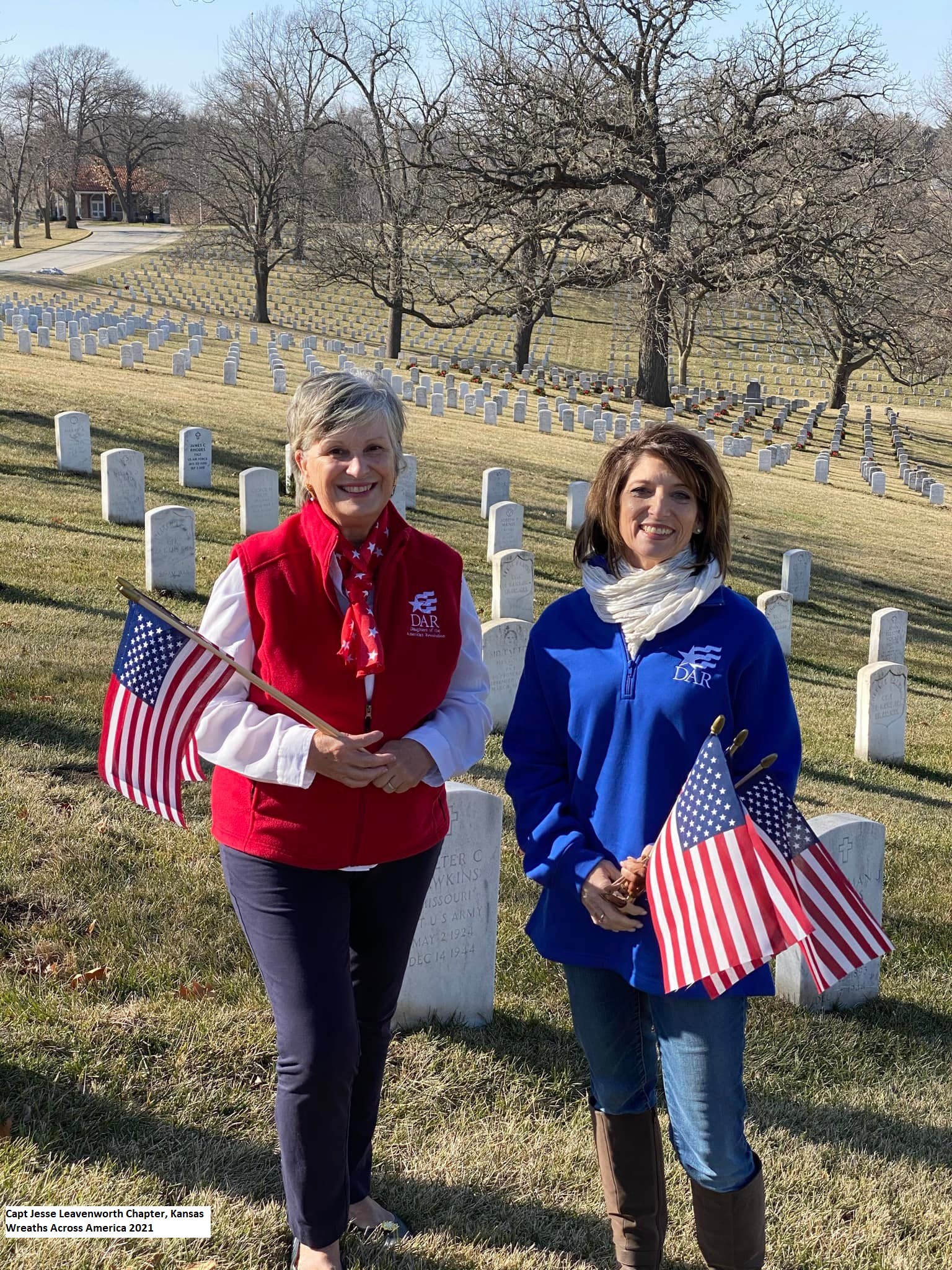 DAR members hold American flags while honoring veterans at a national cemetery service project.