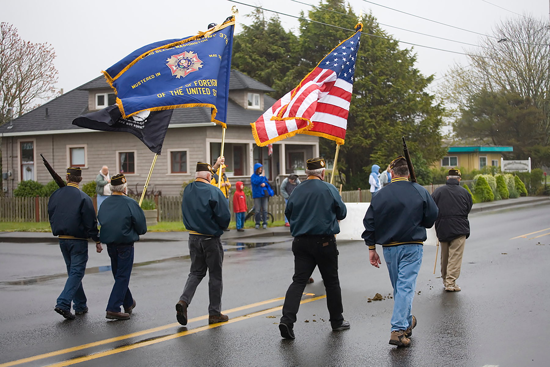 Veterans carry flags in a parade on a rainy day, honoring service and fostering community remembrance.